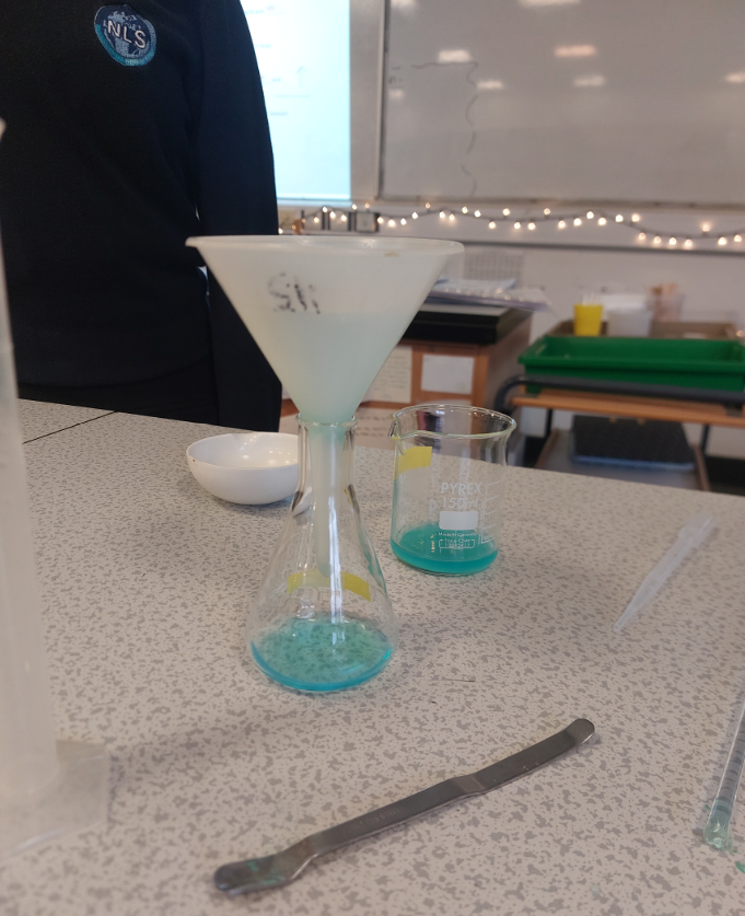 A beaker and a conical flask with a funnel both with blue liquid on a table