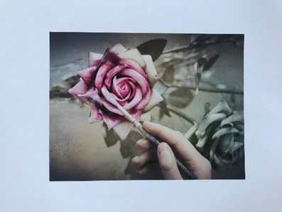 A hand holding a paintbrush painting a rose