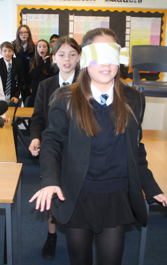 Students taking part in events in the oracy day   - one being guided walking wearing a  blindfold 