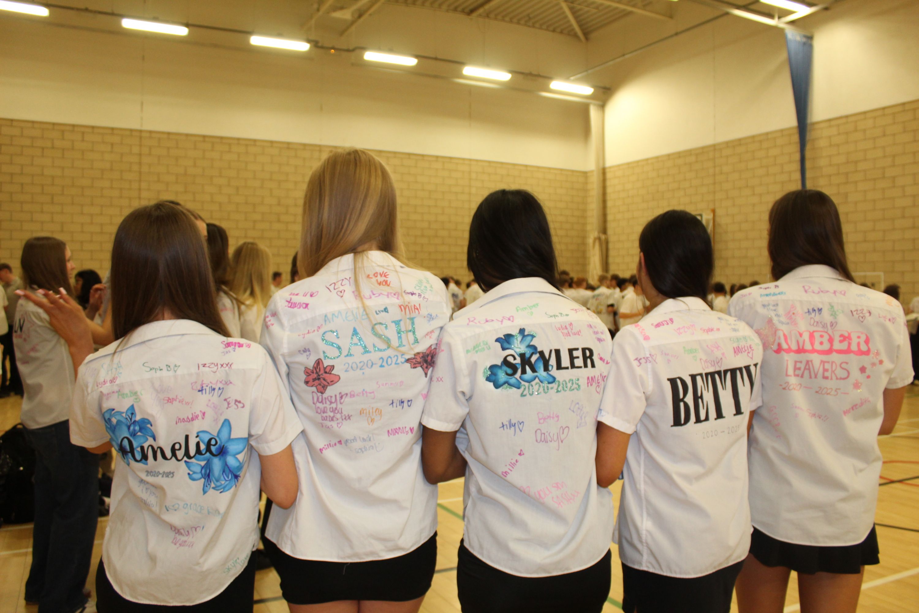Five studnets showing the backs of their shirts with their names and signings