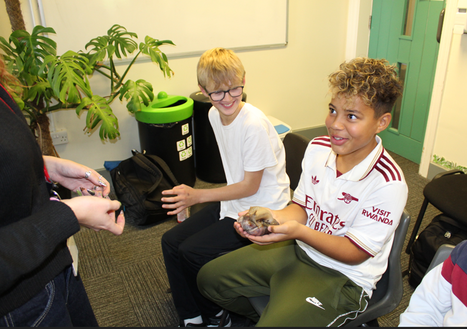 a student holding a giant snail and another student watching