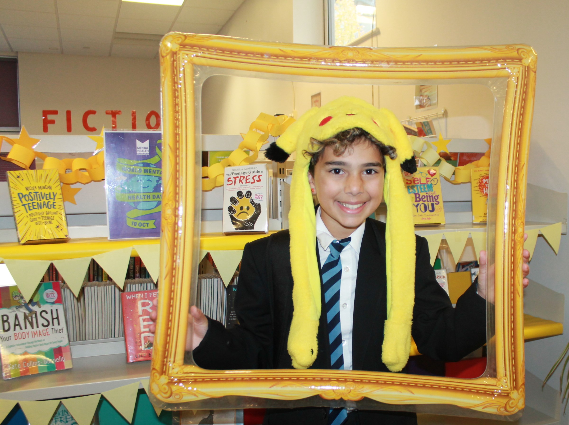 Photo of a student wearing a funny yellow hat behind a golden inflatable picture frame