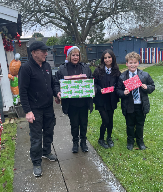 Two students giving a Christmas hamper to a man and woman  in a garden