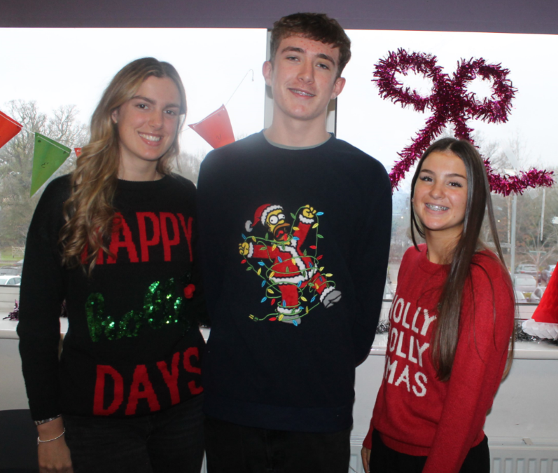 Three Sixth Form students wearing Christmas jumpers in front of a window and Christmas decorations